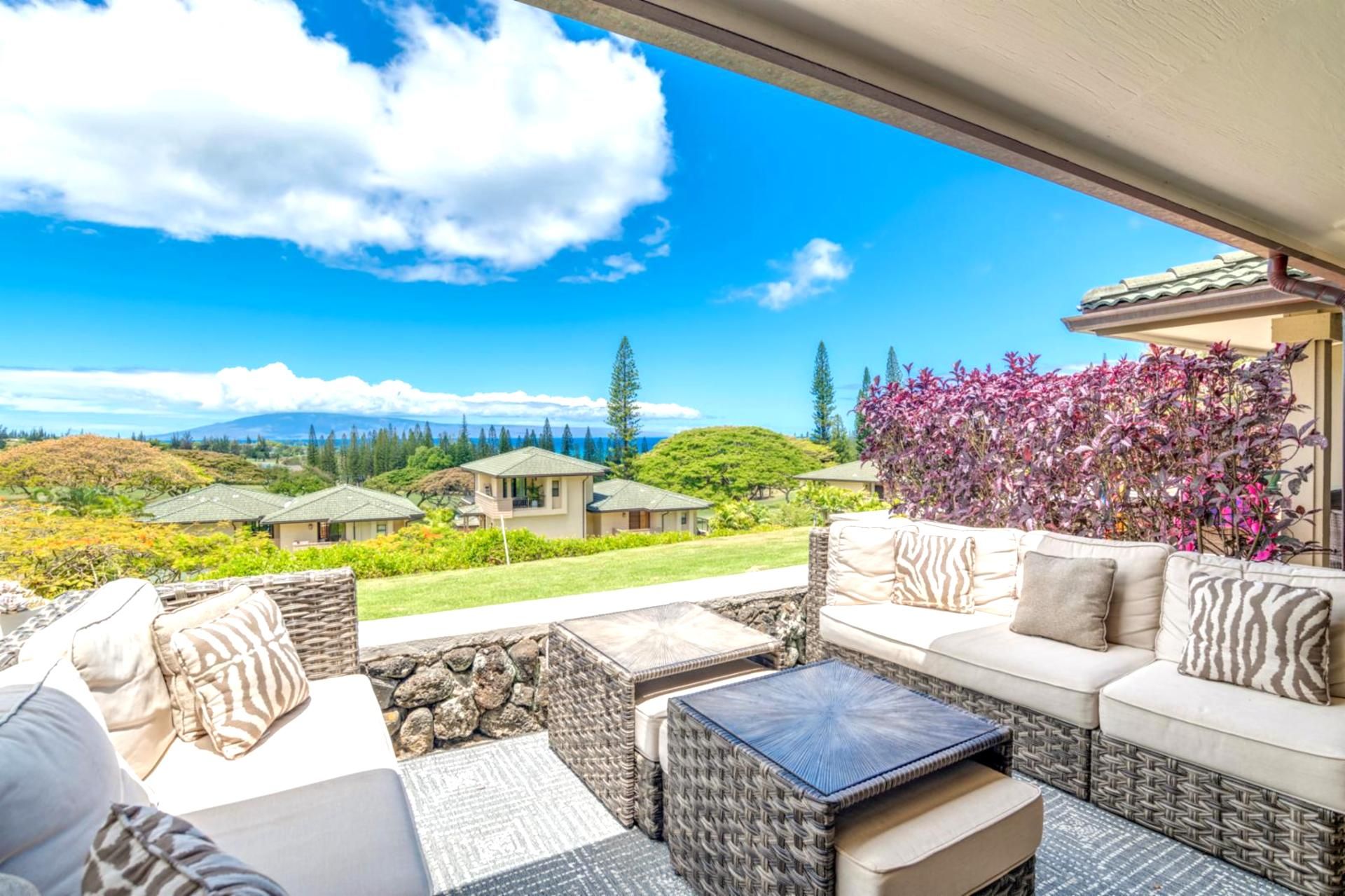 A patio with wicker furniture, a stone table, and a view of houses and mountains.