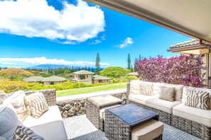 A patio with wicker furniture, a stone table, and a view of houses and mountains.