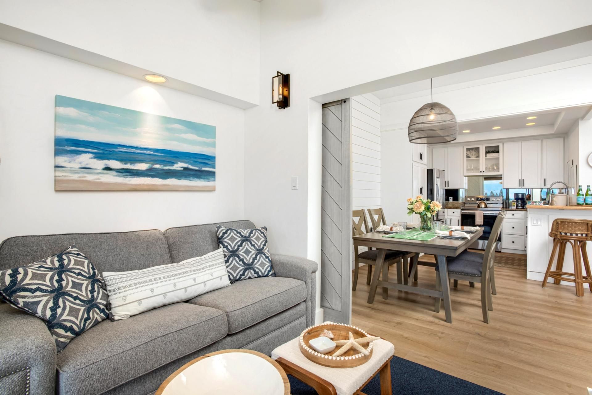 A modern living room with a grey sofa, a dining area with a wooden table, and a kitchen in the background.