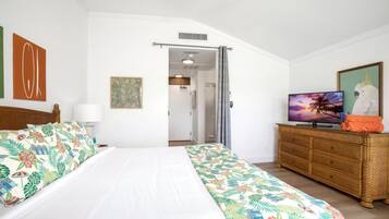 Un dormitorio con cama, televisor, cómoda y puerta que da a un baño.