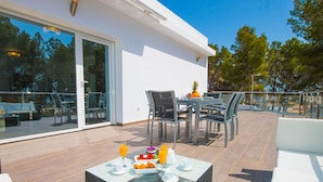 Un espace repas extérieur moderne, avec une table en verre pour deux personnes, entourée de chaises.