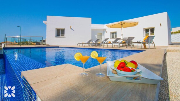 Un espace aménagé au bord de la piscine, avec une piscine à l’eau d’un bleu limpide, des chaises longues et une table sur laquelle se trouvent un saladier rempli de fruits et des boissons.