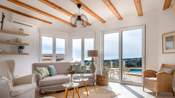 A spacious living room with a sofa, armchairs, a glass coffee table, and a view of a pool through large windows.