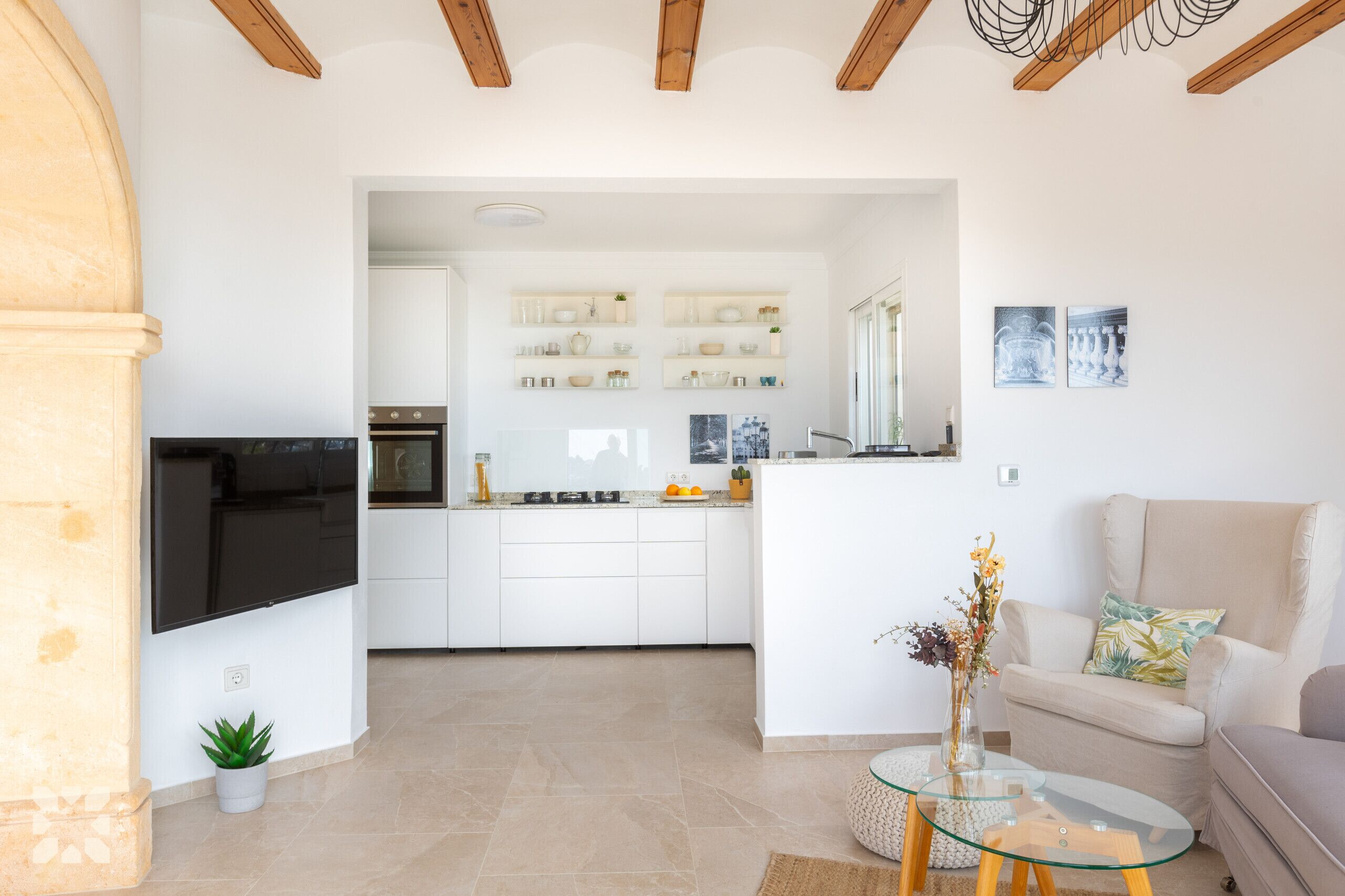 A modern kitchen with white cabinets, a built-in oven, and a glass island with a vase.