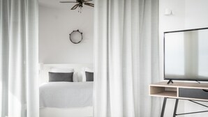 A modern bedroom with a bed, a TV on a wooden stand, and a ceiling fan.