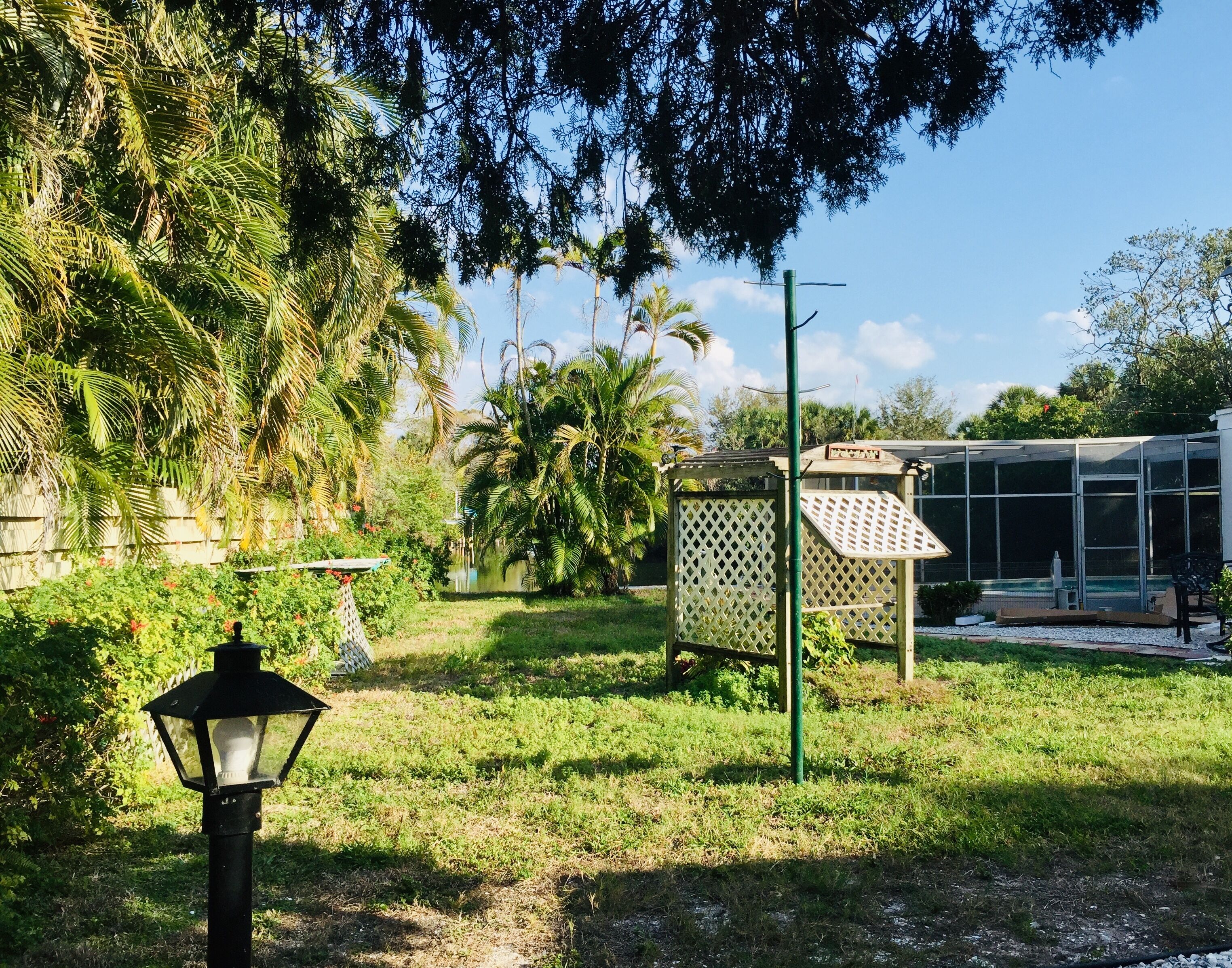 A garden with a pathway, a lamp post, a greenhouse, and various trees.