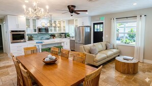 A modern kitchen with white cabinets, stainless steel appliances, and a dining area with a wooden table and chairs. - Sea Whisper: North End gem w/ pool & dock (Anna Maria)