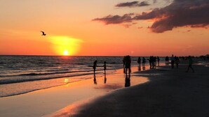 A beach scene at sunset with people walking along the shore. - Sea Whisper: North End gem w/ pool & dock (Anna Maria)