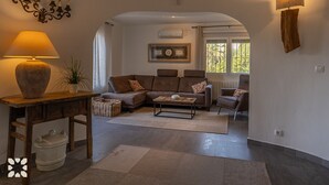 A cozy living room with a sofa, armchairs, a coffee table, a lamp, and a decorative wall piece. - Villa MARIPOSA by Abahana Villas (Benissa)