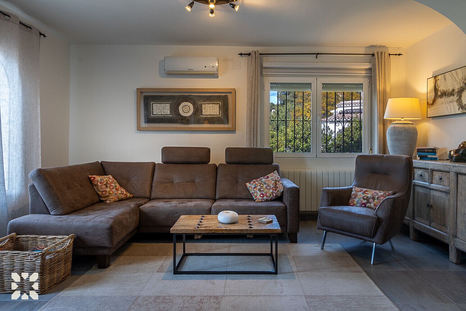 Un salon comprenant un canapé, un fauteuil et une table basse, une fenêtre donnant sur un beau paysage et une lampe.