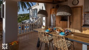 A dining area with wicker chairs, a wooden table, and a view of a house and palm trees. - Villa MARIPOSA by Abahana Villas (Benissa)