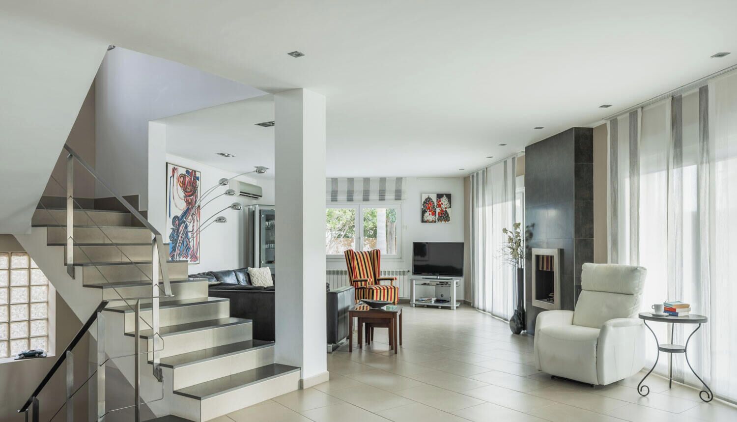 Una sala de estar moderna con una escalera, un televisor de pantalla plana, una chimenea y ventanas amplias.