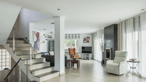 Uma sala de estar moderna com escada, televisão de tela plana, lareira e janelas amplas.