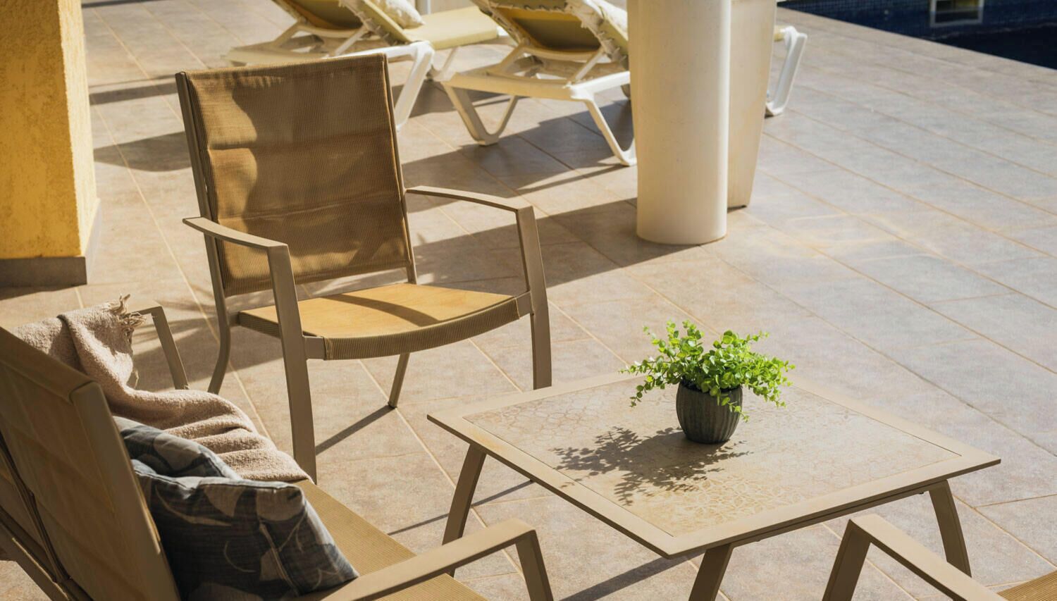 A sunlit outdoor seating area with a table, chairs, and a potted plant.