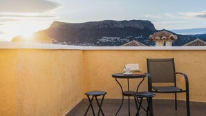 Uma varanda com mesa e cadeiras, com vista para uma paisagem montanhosa.