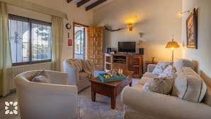 Ein Wohnzimmer mit Sofa, Sessel, Couchtisch aus Holz, Fernseher und Lampe.