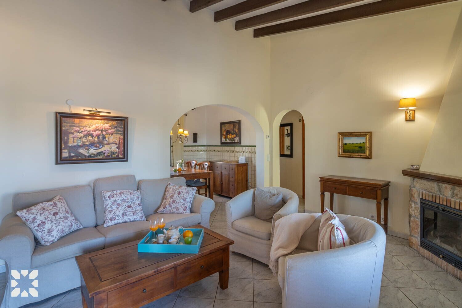 A cozy living room with a sofa, armchair, and coffee table. There is a fireplace and a kitchen area in the background.