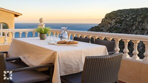 Una mesa con jarras, vasos y pan en un balcón con vista al mar.