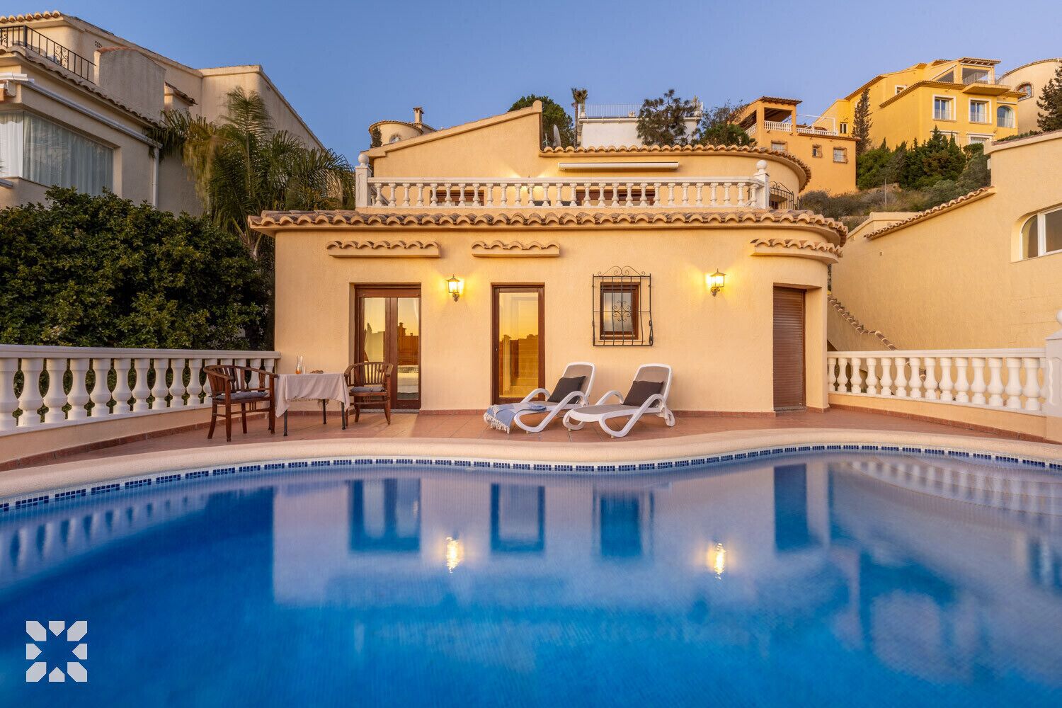 Un espace aménagé au bord de la piscine, avec des chaises longues, une table et un escalier menant à un balcon.