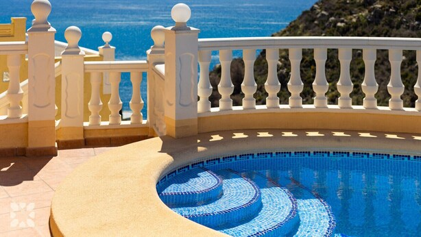 Una piscina con diseño circular, barandilla blanca y vista al mar.
