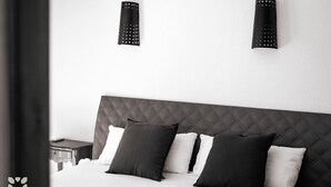 Un dormitorio moderno con cabecera acolchada, cama con varios almohadones y dos lámparas de pared.