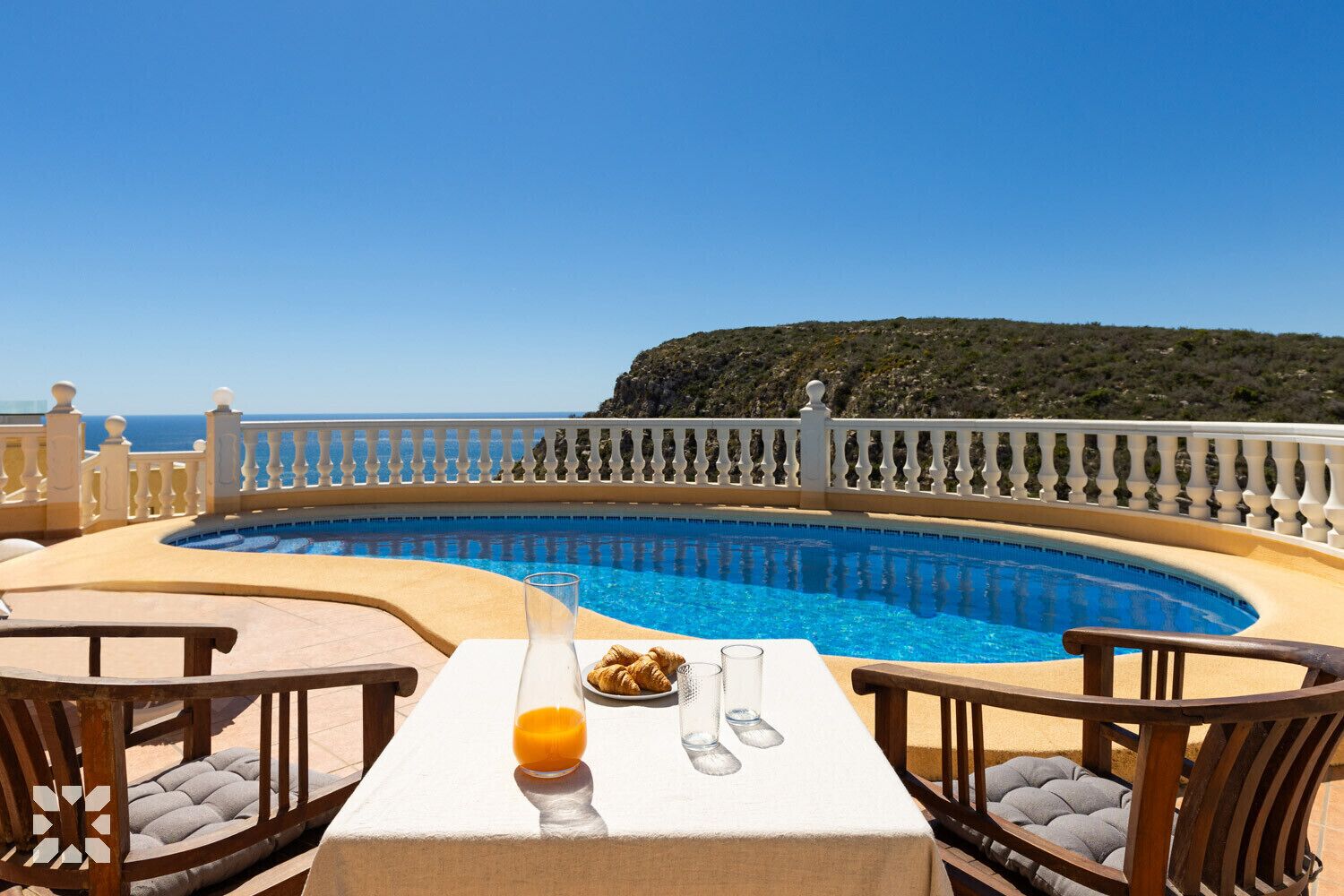A poolside dining area with a table, chairs, and a glass of orange juice.