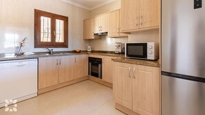 Una cocina con armarios de madera, un refrigerador de acero inoxidable, un microondas, un lavavajillas y un ventanal con reja decorativa.