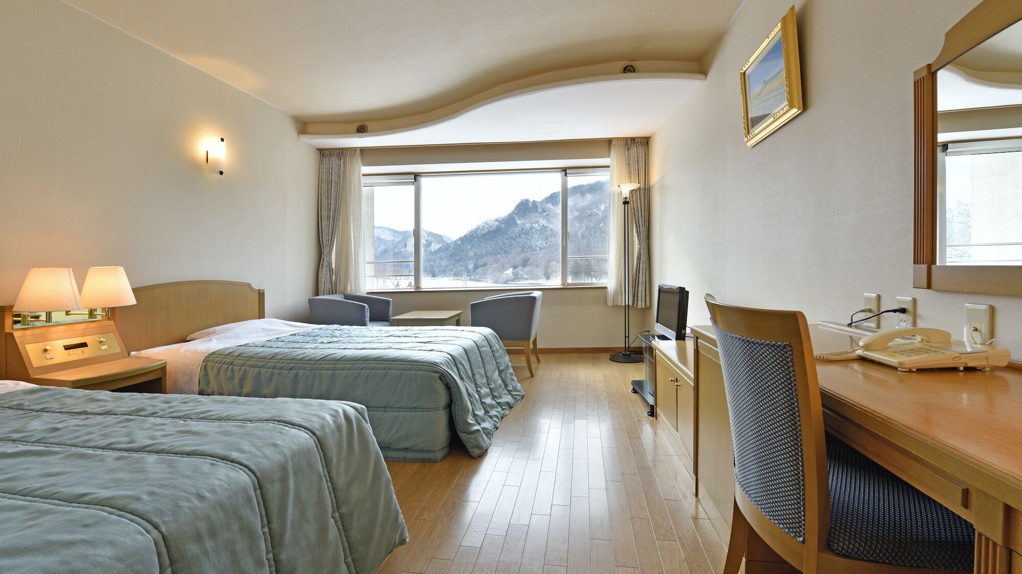 A hotel room with two beds, a desk, a chair, a TV, and a telephone.
