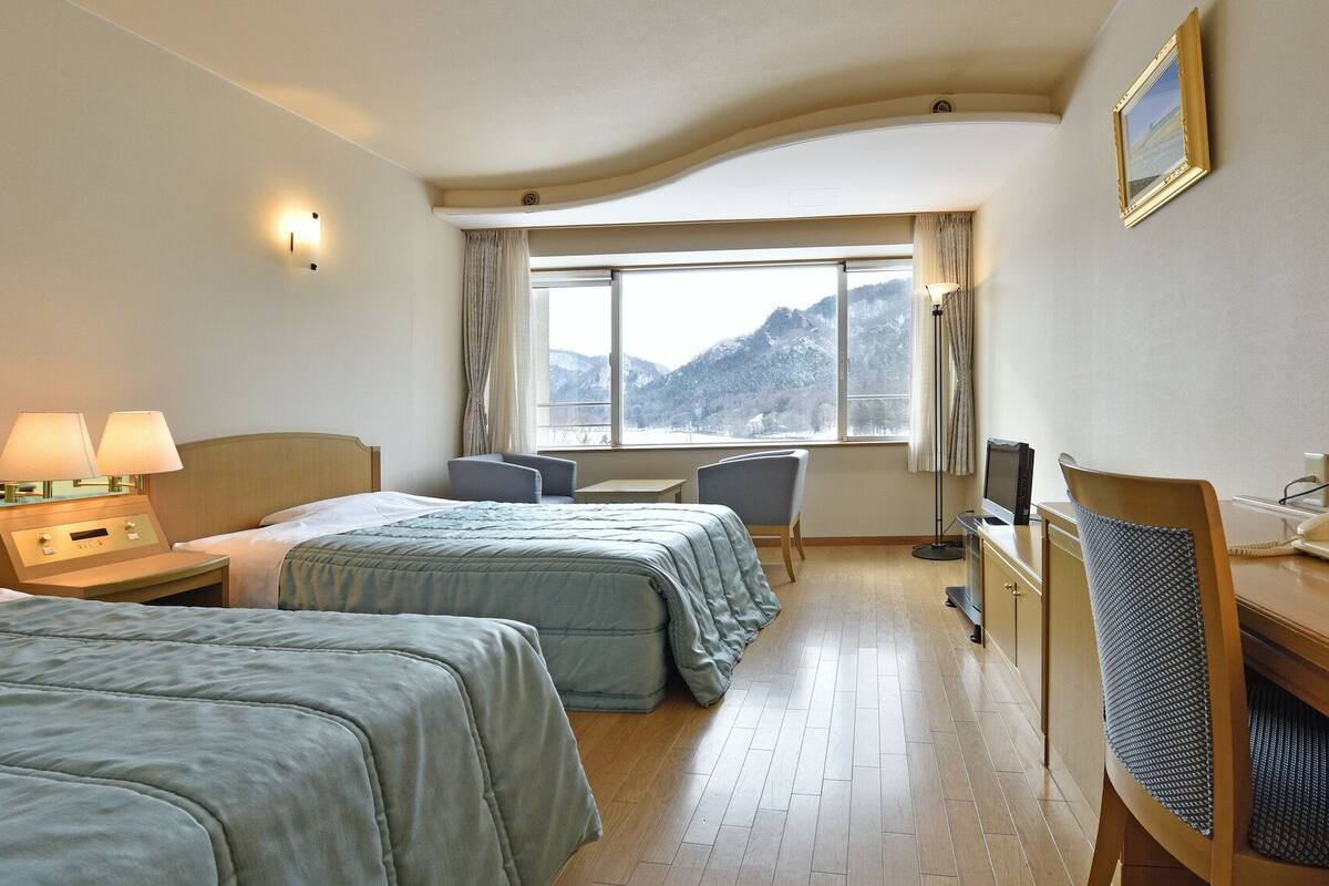 A hotel room with two beds, a desk, a chair, a TV, and a telephone.