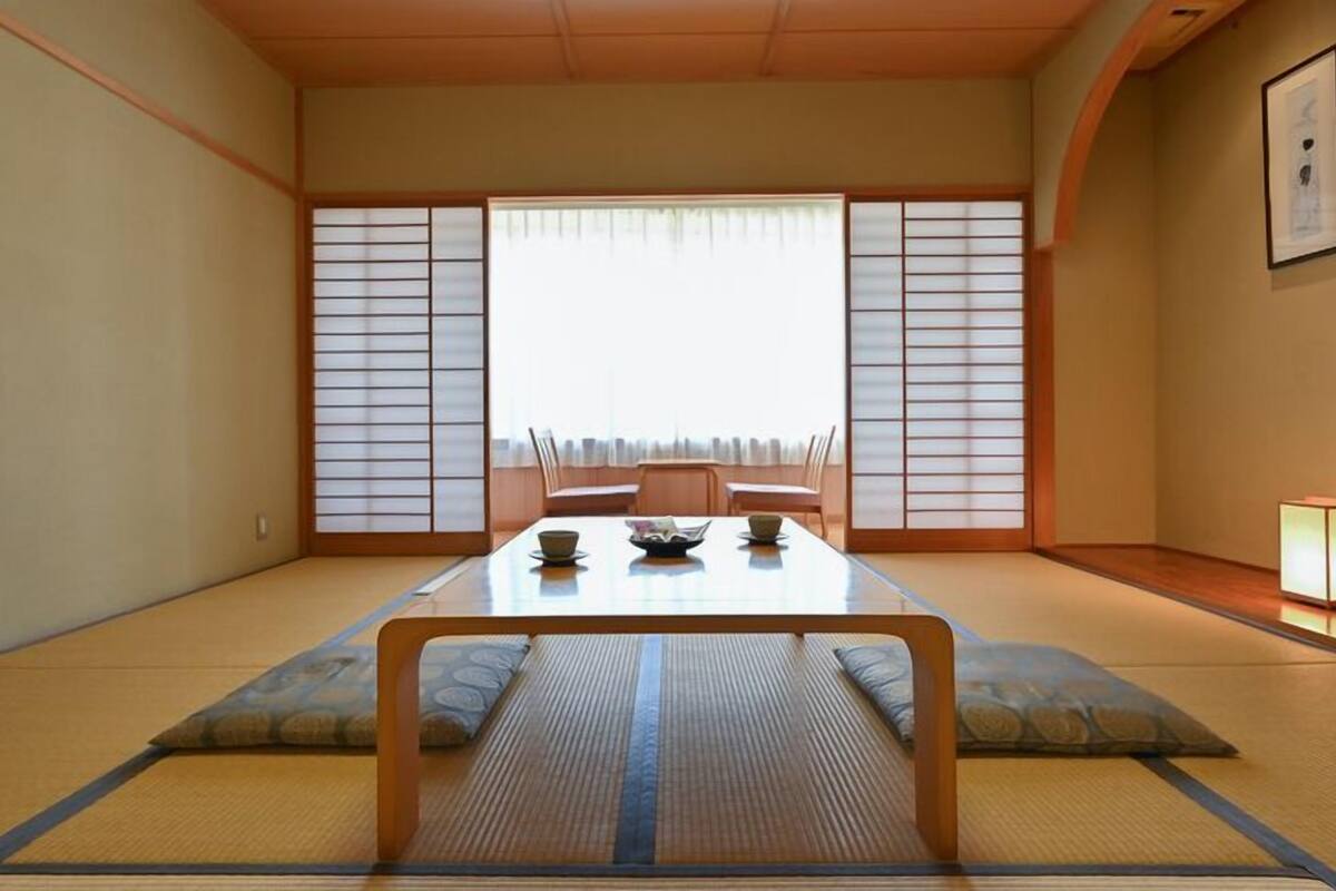 A traditional Japanese room with tatami flooring, a low table with cushions, sliding doors, and a framed picture on the wall.