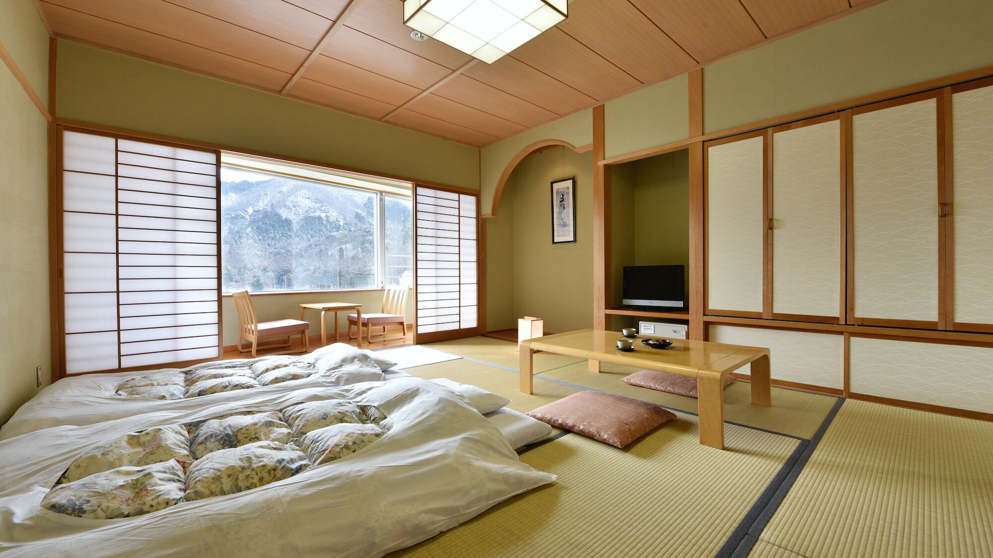 A traditional Japanese room with tatami flooring, a bed with floral bedding, a TV, and a sliding door.