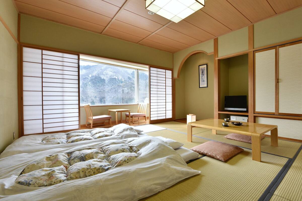 A traditional Japanese room with tatami flooring, a bed with floral bedding, a TV, and a sliding door.