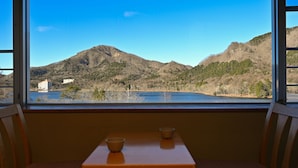 A room with a view of a lake, mountains, and a building across the water. There is a table with two bowls on it. - Yusuge' Lake Haruna SPA Ryokan (Takasaki)