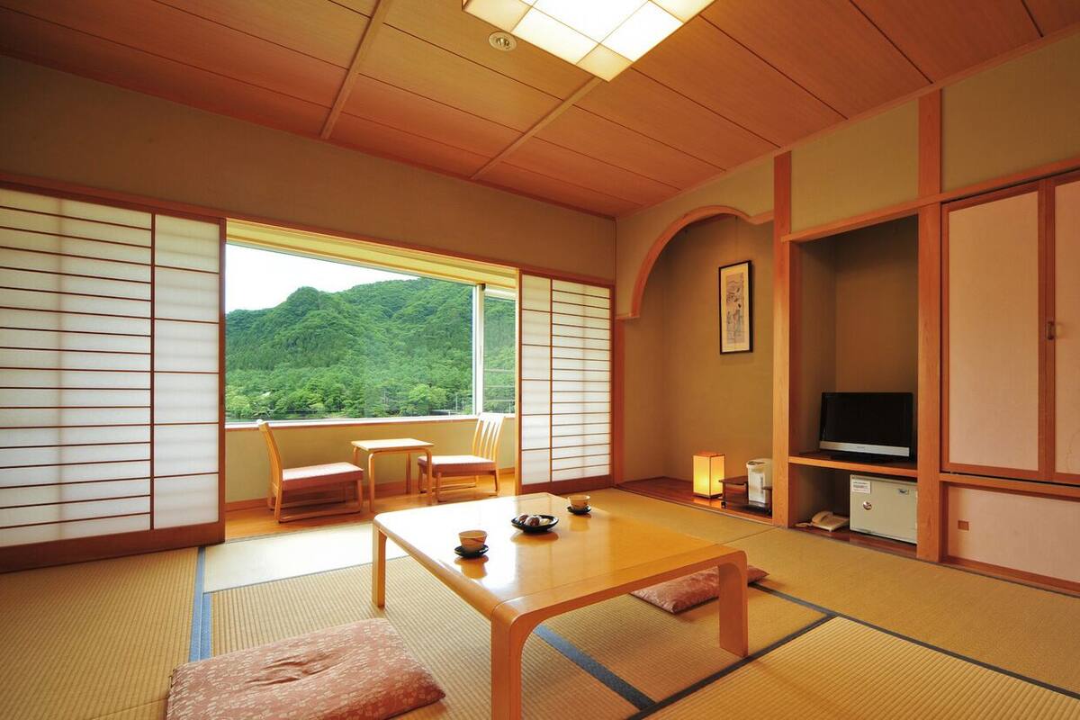 A traditional Japanese room with tatami flooring, a low table, a TV, and a view of a mountain.