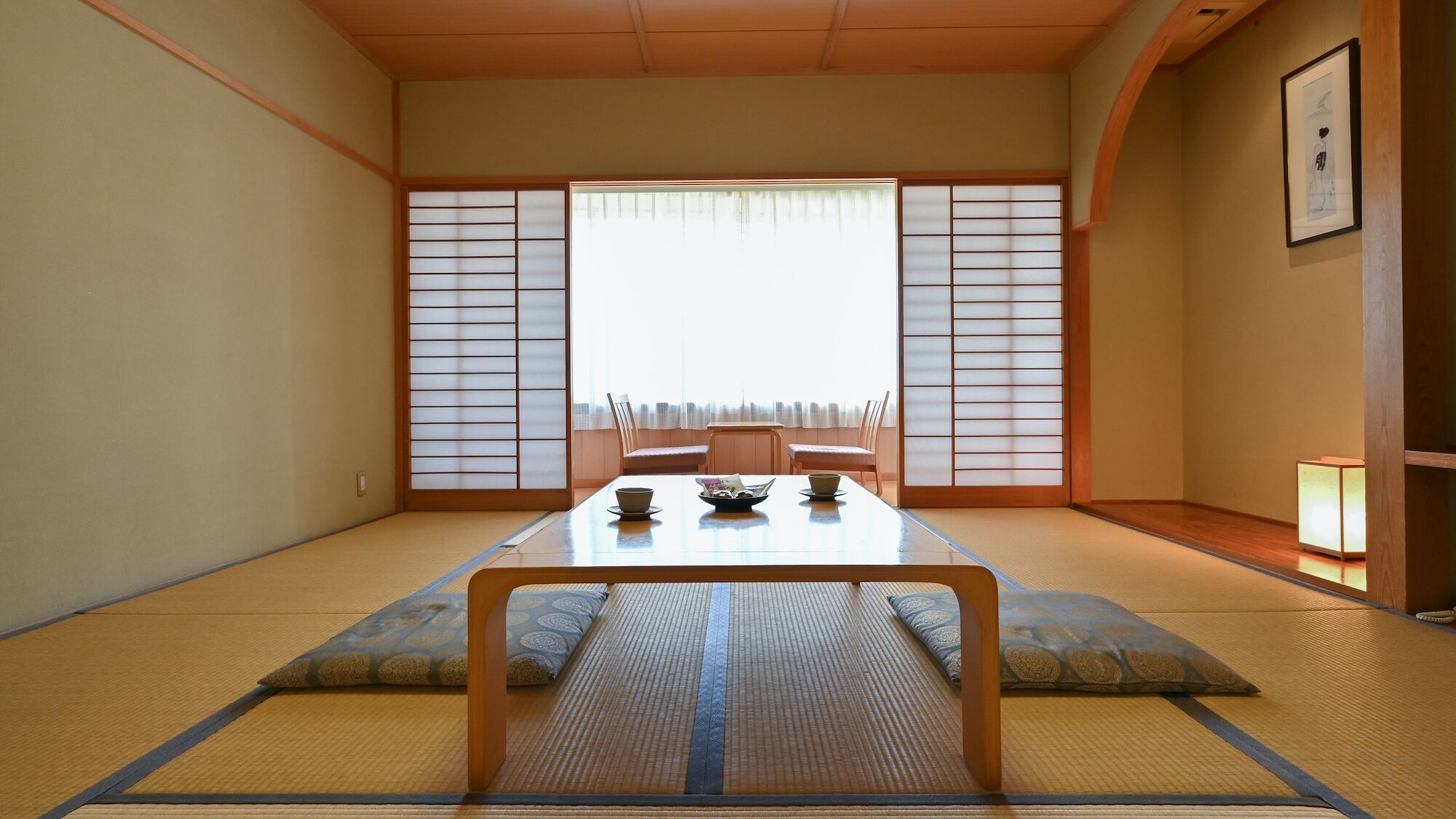 A traditional Japanese room with tatami flooring, a low table with a bowl and chopsticks, and shoji screens.