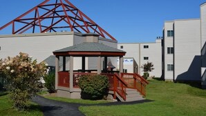 Un edificio con estructura metálica roja, un espacio al aire libre techado y una escalera, y un camino que lleva a la entrada.