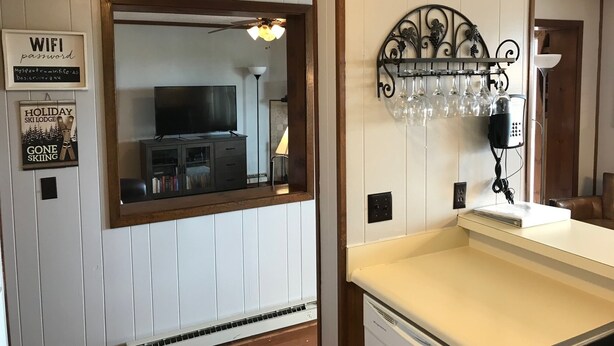 Una habitación con televisión, ventilador de techo, botellero en la pared y un cartel enmarcado con la contraseña de WiFi.