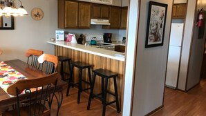 Una cocina con armarios de madera, encimera blanca y una zona de bar con taburetes.