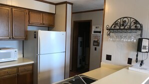 Una cocina con armarios de madera, un refrigerador blanco, un microondas, un lavamanos con dispensador de jabón y una estantería para vinos con copas.