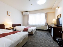 Habitación de hotel con dos camas, un escritorio, una silla, un televisor y una ventana con cortinas.