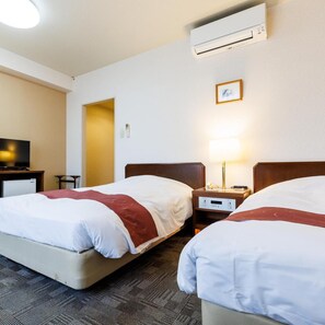 A hotel room with two beds, a desk with a television, an air conditioning unit, and a bedside lamp.