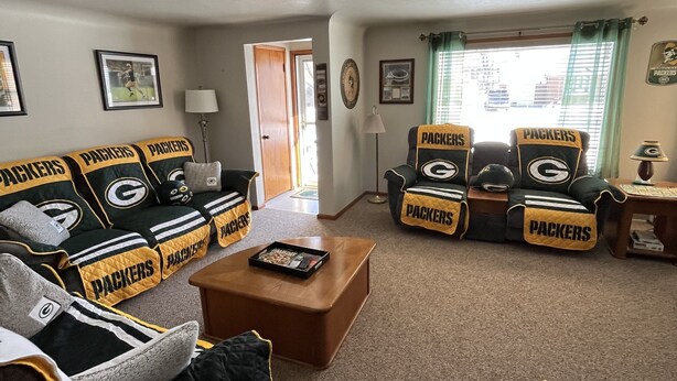 A living room with a couch and chairs covered in Packers merchandise. - In the shadows of Lambeau Field is our Packer House (Green Bay)