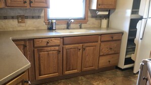 A kitchen with wooden cabinets, a window with a checkered curtain, a sink, and a refrigerator. - In the shadows of Lambeau Field is our Packer House (Green Bay)