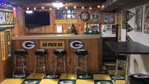 A bar area with a checkered floor, bar stools, a counter with a 'Go Pack Go' sign, and various sports memorabilia on the walls. - In the shadows of Lambeau Field is our Packer House (Green Bay)