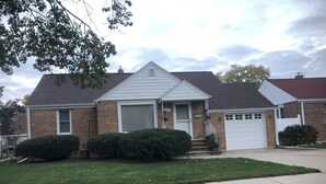 A two-story house with a front porch, a garage, and a well-maintained lawn. - In the shadows of Lambeau Field is our Packer House (Green Bay)