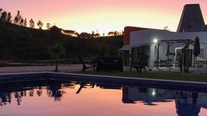 A swimming pool with a clear reflection, a covered outdoor seating area, and a building with a modern design. - A.ti.tudo Nature (Portimão)