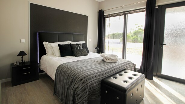 A modern bedroom with a large bed, a bedside table, a lamp, and a view through a large window. - A.ti.tudo Nature (Portimão)