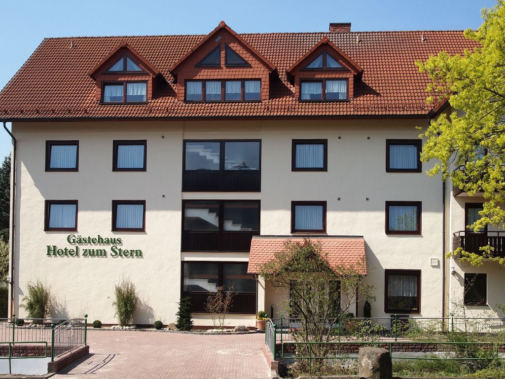 Un hotel de dos plantas con tejado de tejas rojas y un letrero que dice 'Gästehaus Hotel zum Stern'.