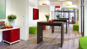 A modern hotel lobby with a wooden floor, green and red seating, a reception desk, and pendant lighting. - Parkhotel zum Stern (Oberaula)