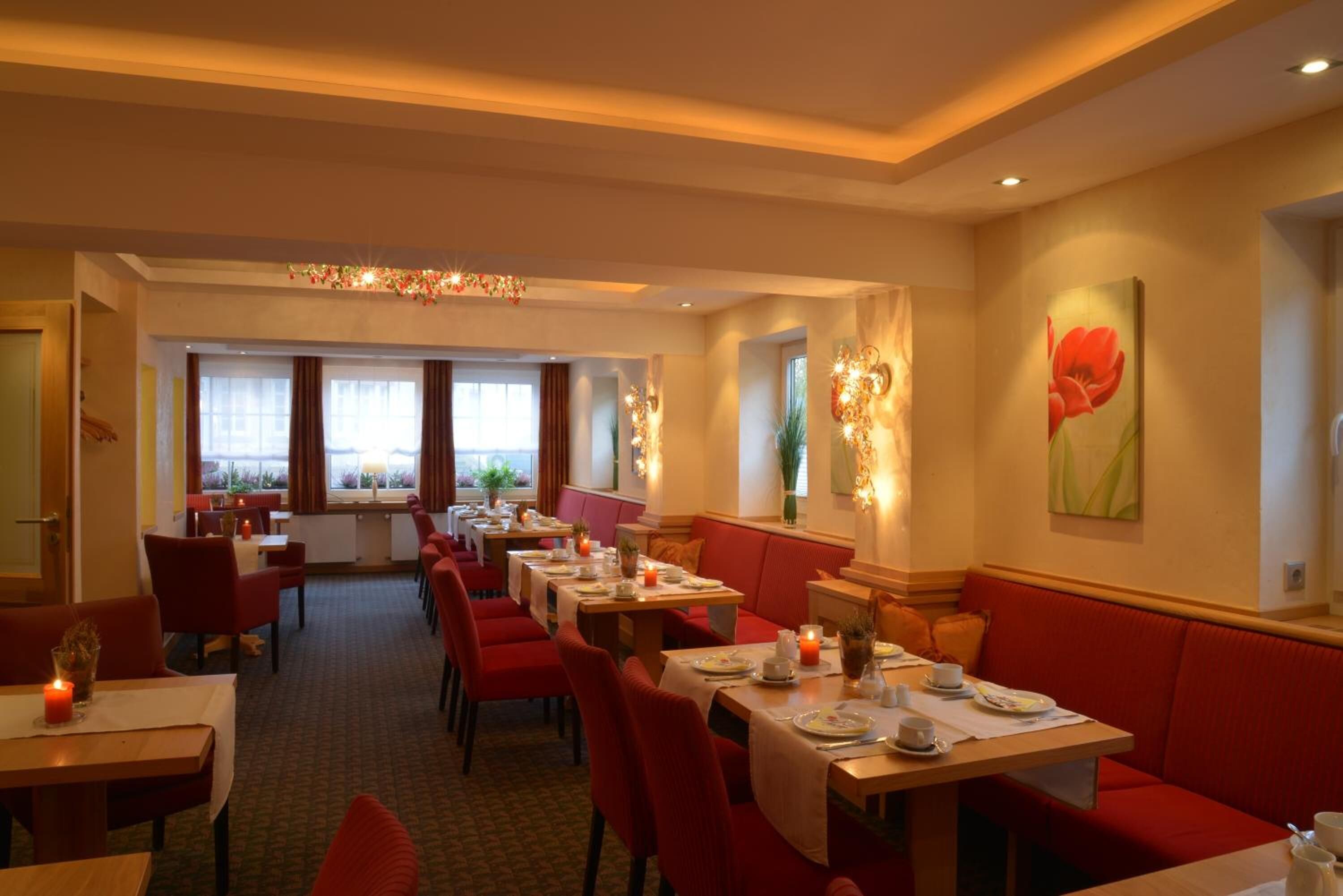 Un restaurante con asientos tipo banca rojos, mesas, iluminación cálida y ventanas amplias.